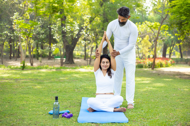 印度男老师或教练在公园里教年轻的女学生瑜伽，两人一起在户外做伸展健身运动，运动和锻炼的概念。图片下载
