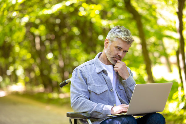 白发苍苍的残疾自由职业者坐在轮椅上在线工作。图片下载