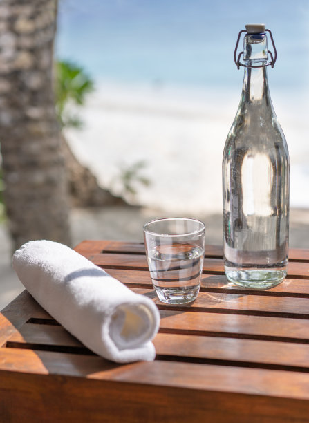 马尔代夫海滩的背景是玻璃瓶、卷起的毛巾和一杯水图片下载