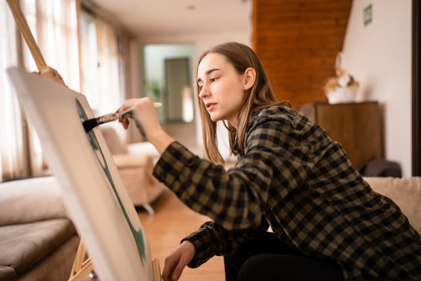 一位年轻美丽的白人女性艺术家坐在床上沙发在画布上绘画，拿着画笔艺术和创意专业或爱好概念真实的人侧视复制空间图片下载