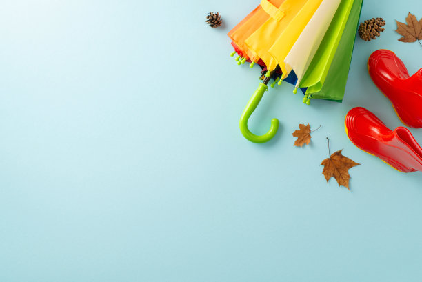 秋天的仙境。俯视图以儿童的红色口香糖鞋，彩虹图案的充满活力的雨伞，散落的树叶，松果在柔和的蓝色背景下，为文本或促销内容提供空间图片下载