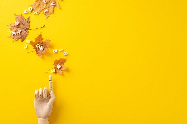 在这个俯视图中发现一个学习的世界。一个木制假人的手指着鲜艳的黄色背景上飞舞着金色枫叶的字母，等待着你的文字或广告图片下载
