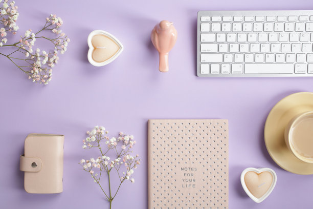 舒适的家庭办公室办公桌与键盘，笔记本，咖啡杯，配件和石膏花在粉彩紫色的背景。优雅女性的工作区。平铺，俯视图。图片下载