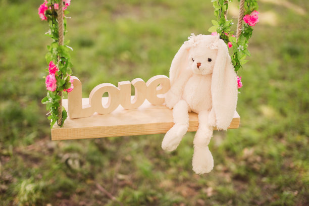 可爱的兔子玩具和木制的爱装饰在一个用花装饰的秋千。图片下载