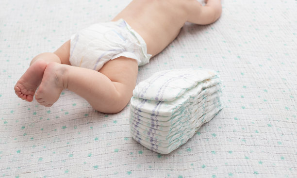 一个穿着尿布的婴儿的腿，背景是一堆儿童舒适的尿布，特写。文本复制空间图片下载