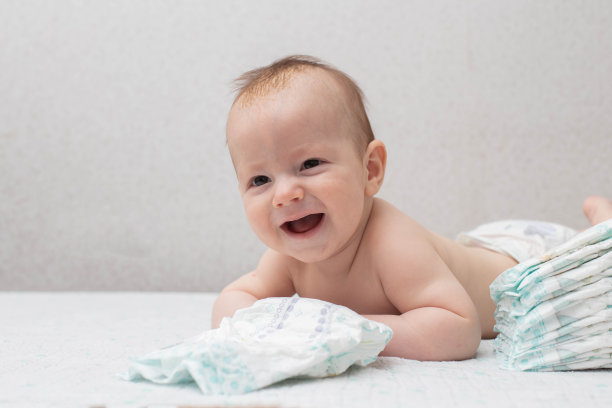 一个5个月大的小男孩躺在白色背景上的尿布里，看着镜头。叠放纸尿裤，防漏，柔软舒适。文本复制空间图片下载