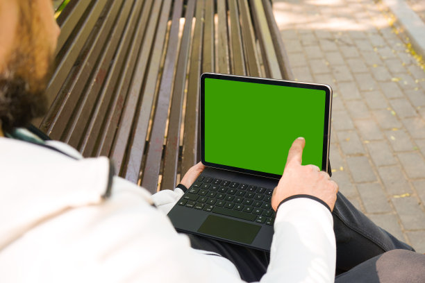 一名自由职业者手持黑色平板电脑，模拟绿色桌面屏幕，坐在公园的长凳上图片下载