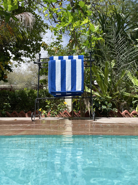 特写图片池边独立式金属毛巾架，阳光下的蓝白条纹毛巾，池边石天井方板，室外，游泳池用绿松石蓝色马赛克瓷砖被波纹水扭曲，溅起的水，重点在前景图片下载