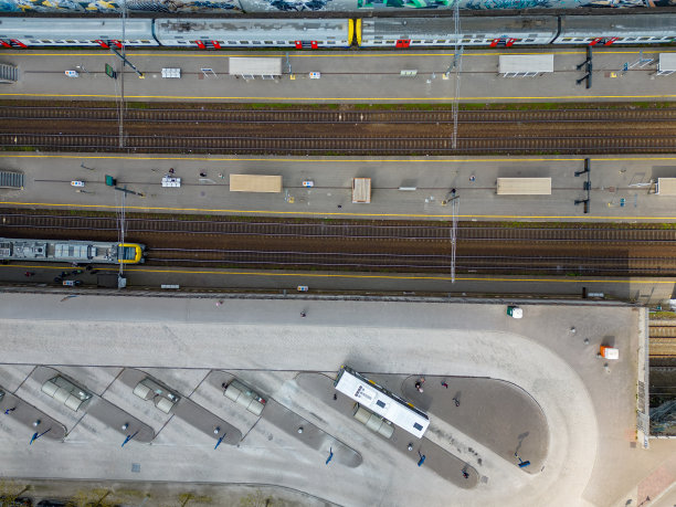 从空中俯瞰的火车站交通枢纽照片，显示不同的火车并排停在站台旁边的轨道上，公共汽车在外面等候。图片下载