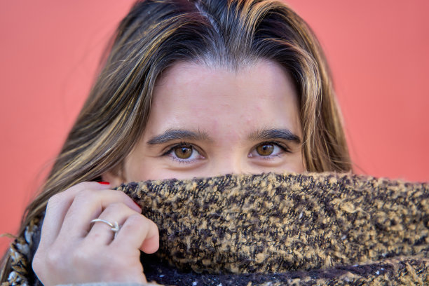 一个女人看着相机的肖像，她戴着羊毛帽子，用围巾遮住了她的嘴，在红色的背景上孤立起来图片下载