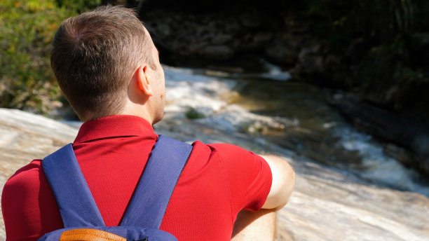 近距离的男性旅行者与背包在他的背上坐在山河附近图片下载