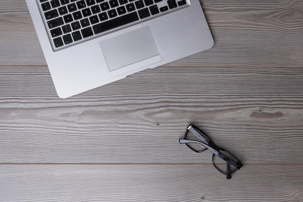 木桌上放着笔记本电脑，眼镜和大片的排版空间。图片下载