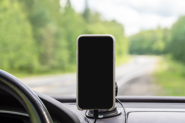 一辆汽车的仪表盘上，以挡风玻璃为背景，屏幕为空白，智能手机放在支架里，后面是道路景观。图片下载