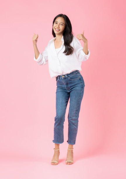 工作室拍摄的开朗美丽的亚洲女人，穿着白衬衫，站在粉红色的背景上，竖起大拇指表示喜欢和赞同。图片下载
