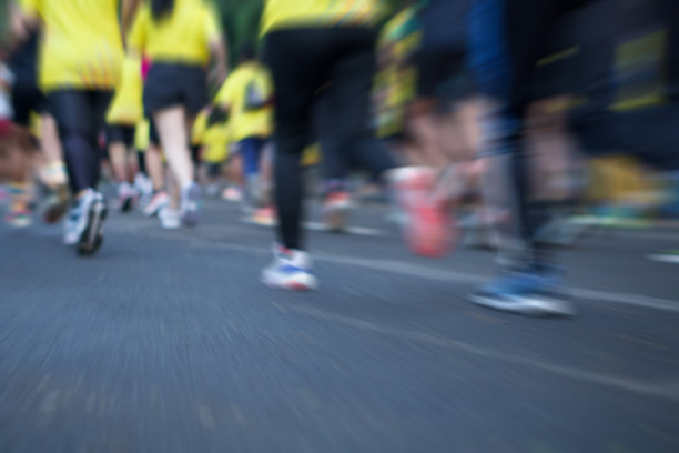 许多穿着黄色衬衫的跑步者在柏油路上跑步的后视图。有选择性的重点。运动模糊图片下载