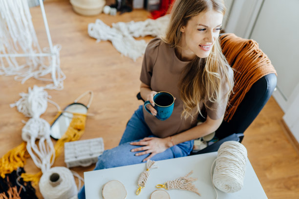 近距离俯视图的女工匠与一杯茶放松在一个家庭工作室编织车间。图片下载