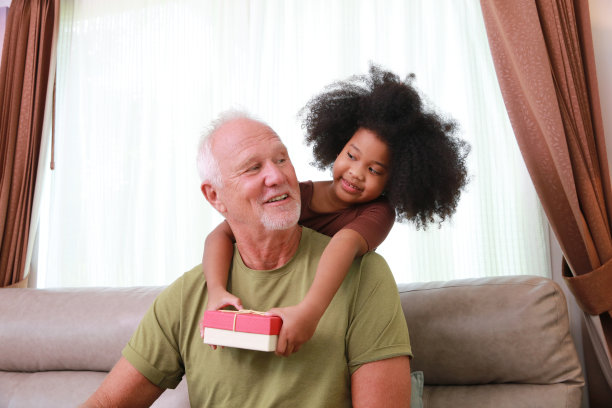 小女孩从背后拥抱爷爷，并给他一个可爱的礼盒图片下载