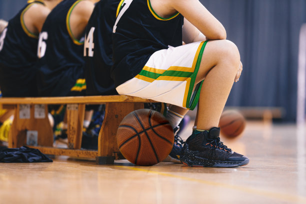 篮球运动员坐在木凳上。一群十几岁的男生在球场上观看篮球比赛。孩子们穿着篮球制服作为替补球员图片下载