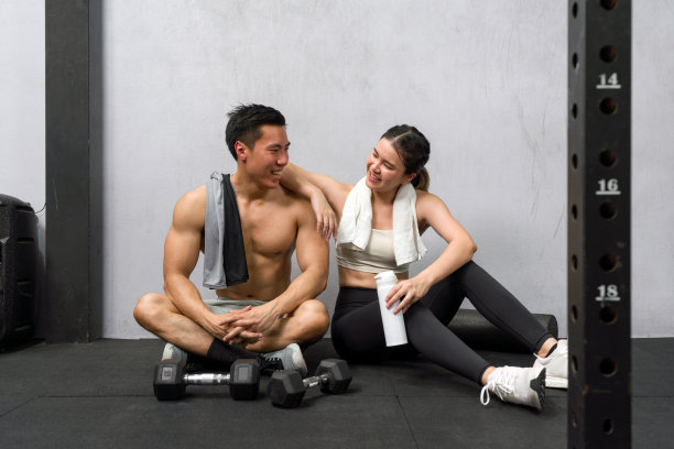 年轻的亚洲夫妇在健身房地板上锻炼，周围是哑铃，从事片刻的休息。图片下载