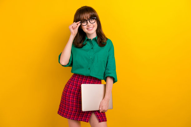 照片的漂亮甜美的女士穿着绿色的衬衫拿着苹果三星现代小工具孤立的黄色背景图片下载