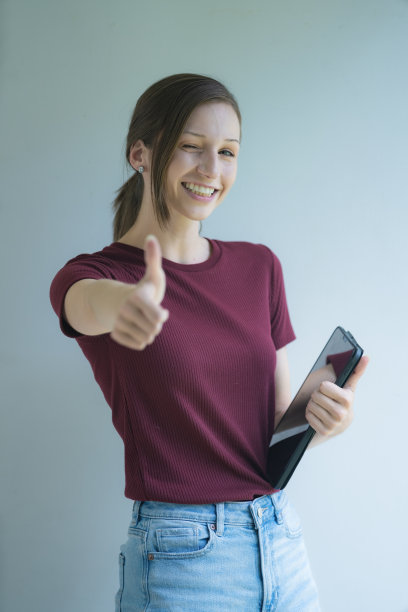一位年轻的白人女性站在白色的背景上，一只手竖起大拇指，手里拿着一块写字板。图片下载