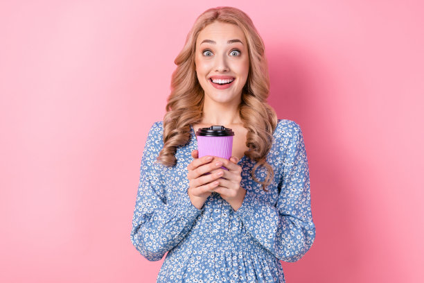年轻的惊讶女子的照片金发波浪发型拿杯新鲜拿铁玛奇朵咖啡饮料外卖孤立在粉红色的背景图片下载