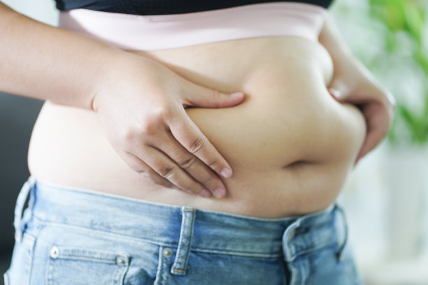 肥胖的女人对她的肚子感到不安。超重的女人抚摸着自己肥胖的肚子，想要减肥。胖女人用紧绷的衣服担心体重节食的生活方式概念图片下载