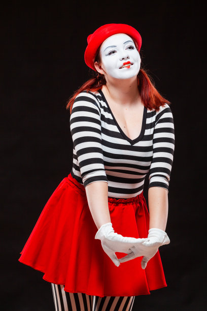 女哑剧艺术家表演的肖像，孤立在黑色背景上。穿着条纹衣服和红色裙子的女人微笑着绞着手图片下载