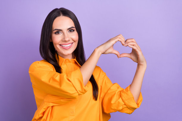 好心情的漂亮女人的肖像，长发，穿着超大衬衫，手指上显示心形符号，孤立在紫色背景上图片下载