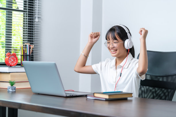 快乐微笑的女学生戴着耳机在家庭办公室用笔记本电脑在线讨论会议。学习远程教育业务的女大学生图片下载