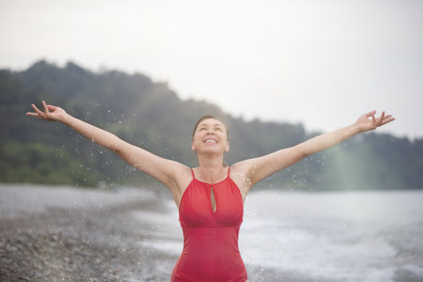 海滩上快乐的中年妇女举起双手，享受着快乐的时刻。图片下载