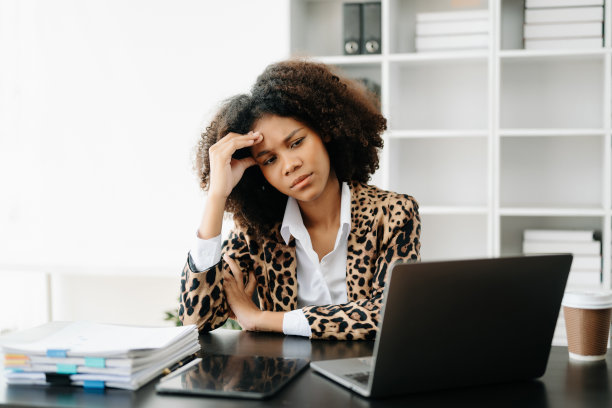 由于在办公室用平板电脑和笔记本电脑工作而感到疲倦和过度思考的非洲妇女。图片下载