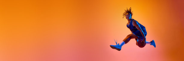 运动的年轻人，篮球运动员，在霓虹灯的橙色背景下跳球图片下载