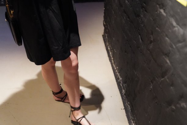 一个年轻的女孩坐在阳台上的木椅上，穿着黑色的裙子，戴着眼镜，手里拿着电话，金色的长发盘成一个髻，绿色的叶子，花朵图片下载