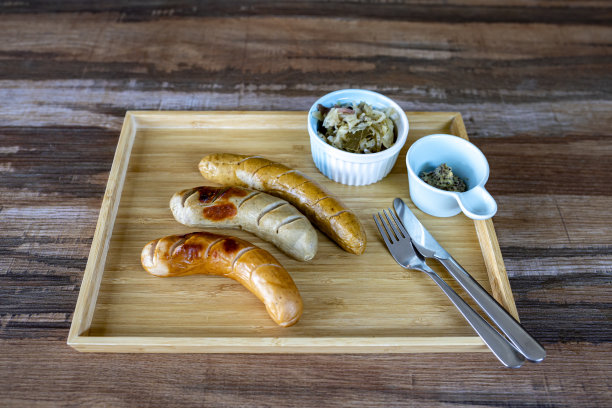 烤德国香肠配酸菜和第戎芥末的照片，放在小碗里，刀叉放在一个长方形的木托盘里，放在木纹桌子上。可以上菜了。有选择性的重点。图片下载