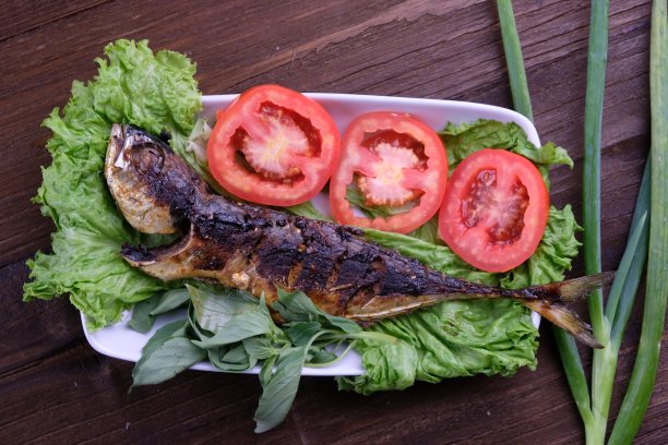 烤鱼和新鲜蔬菜。生菜，番茄片，罗勒叶，葱。印尼的食物。鱼bakar。图片下载