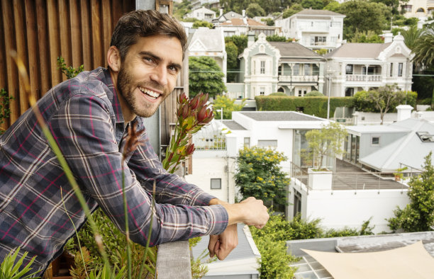 微笑的年轻人倚靠在阳台上，俯瞰着一个风景优美的社区图片下载