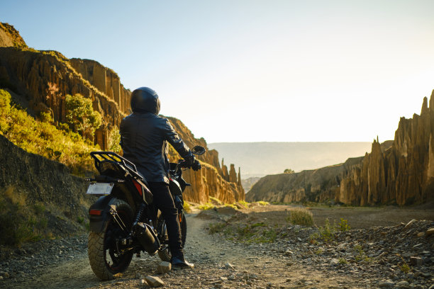 戴着黑色头盔的摩托车手在玻利维亚的日落之旅中休息图片下载