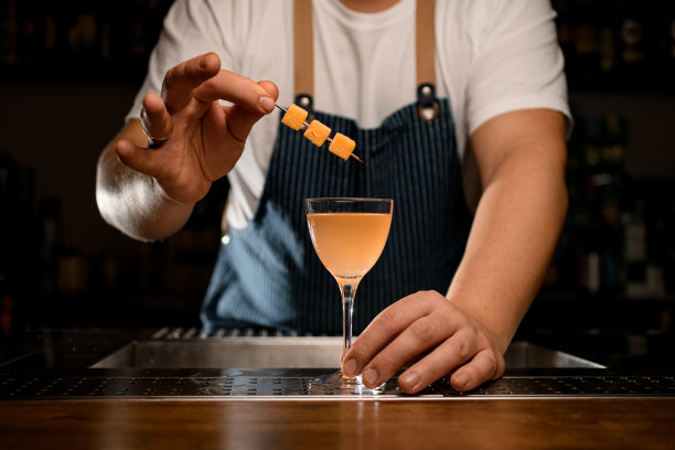 酒吧柜台上，调酒师的手拿着装饰鸡尾酒杯和酒精饮料图片下载