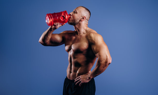 男子健美运动员在蓝色背景上摆姿势。一个人拿着一个装饮料的瓶子。运动营养，食品添加剂。图片下载