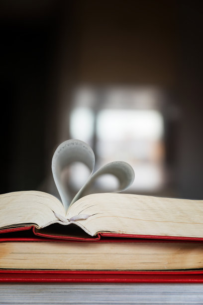 一堆红封面的书。翻开的一本书上，折叠着一颗心。爱书的概念和知识。图片下载