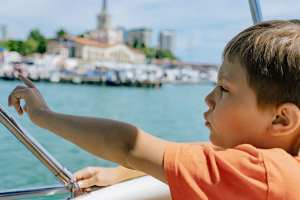 男孩在游艇上航行，指着海港欣赏海景图片下载