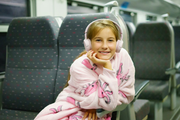 小漂亮女孩坐在火车上旅行。孩子戴着耳机听音乐，看着手机图片下载