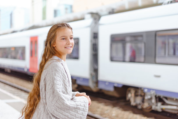 可爱的小女孩提着行李箱在车站等车图片下载