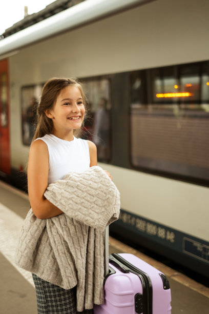 可爱的小女孩提着行李箱在车站等车图片下载