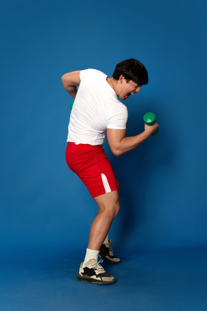 穿着运动服训练的年轻人的全身肖像，带着哑铃，在蓝色的工作室背景下玩耍图片下载