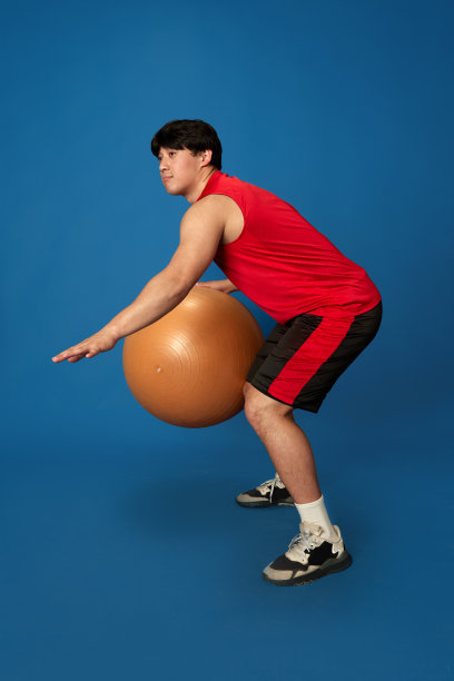 穿着运动服训练的年轻马的全身画像，在蓝色的工作室背景下玩健身球图片下载