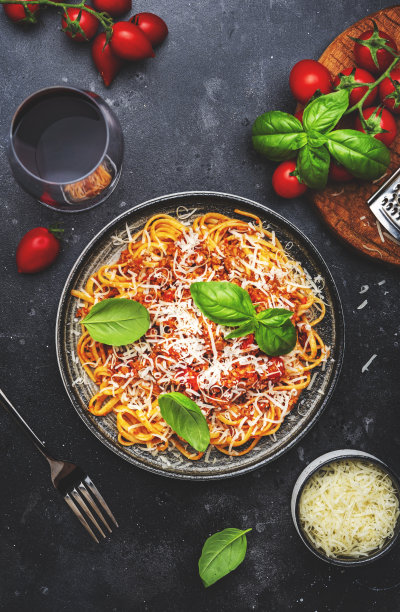 肉酱意大利面或番茄酱肉末意大利面，绿色罗勒撒上磨碎的帕尔马干酪和基安蒂红葡萄酒杯，深色桌，俯视图图片下载
