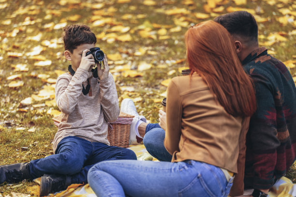 秋天的一天，年轻快乐的父母和他们的儿子在公园里玩耍。男孩给他的父母在野餐时拍了一张照片图片下载