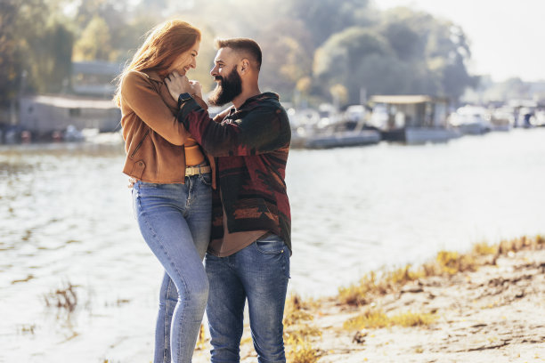 幸福的年轻情侣在河边牵着手散步。图片下载